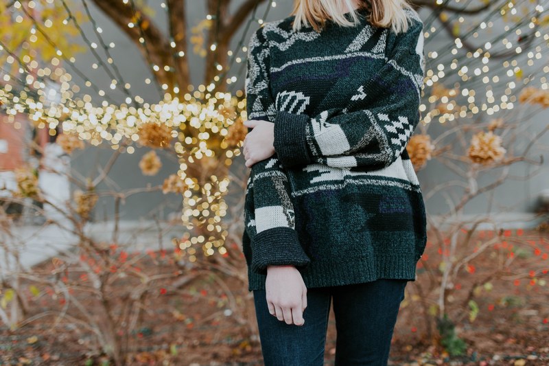 a woman wearing a cozy knit sweater standing in front of fairy lights and trees, woman with trees and lights 4k