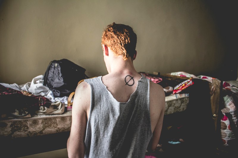 a young man in a tank top standing next to a bunk bed with a backpack on top of it, packing on the bunk bed 4k