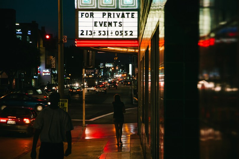 neon sign reflects on sidewalk in downtown area at night near traffic, neon sign at night with cars 4k