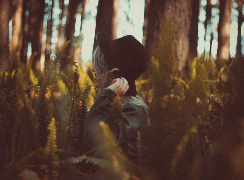 a woman in a hat standing among tall ferns and smiling, woman in tall ferns 4k