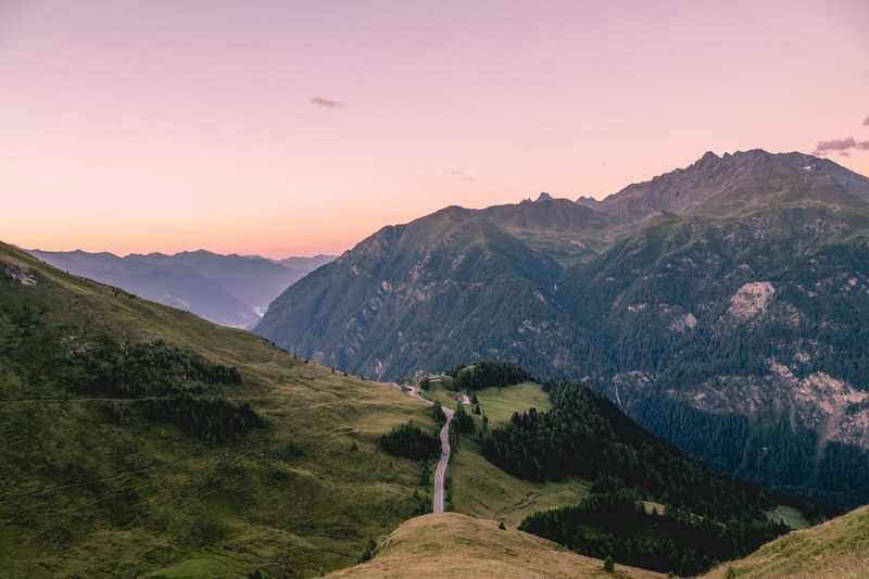 a road running along a green slope in the austrian alps, purple dusk in the alps 4k