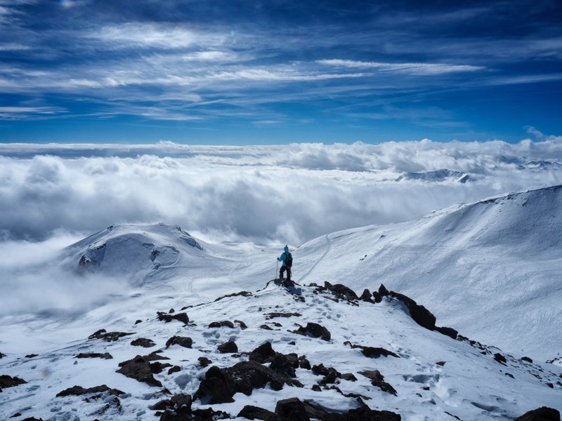 a person standing on top of a mountain staring out into the nearby snow coated mountain peaks, top of a snowy mountain 4k