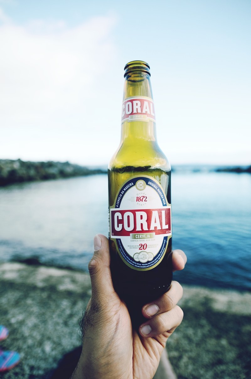 the macro view of a hand holding a beer bottle close to a river, hand holding beer 4k