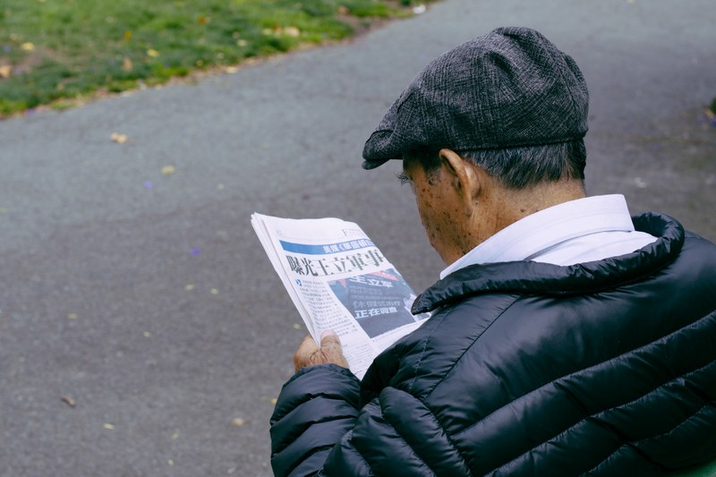 an older chinese man stares down at a newspaper at fishermans wharf, chinese guy reading newspaper 4k