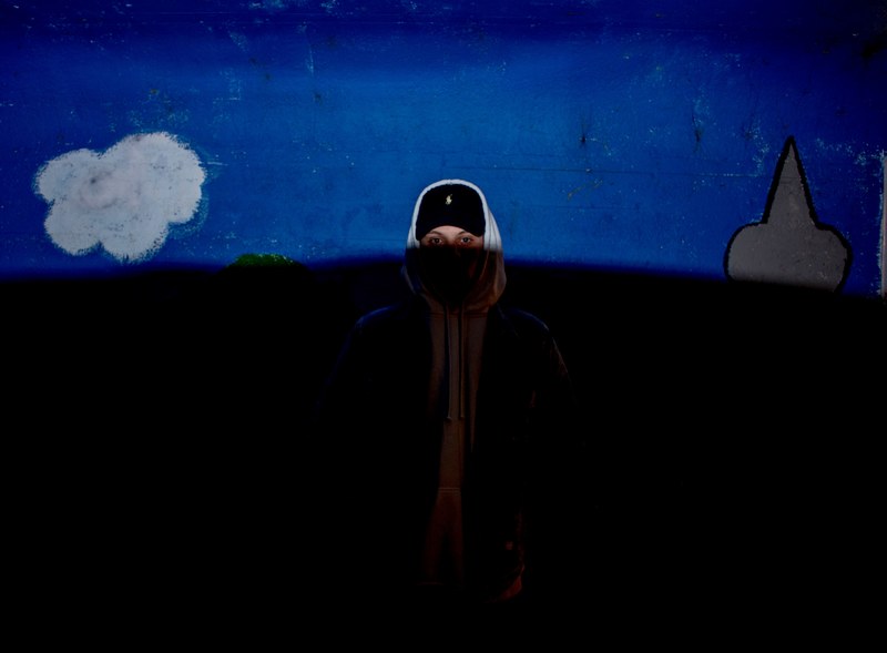 person in a hoodie and hat standing in the shadows with only their face lit, body in the dark 4k