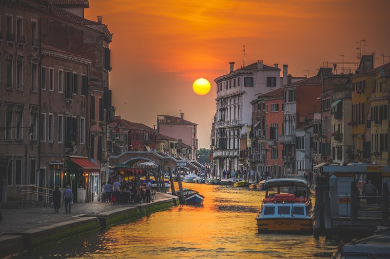 an italian canal bathed in the warm light of the setting sun with a bridge at the back, sunset in venice italy 4k