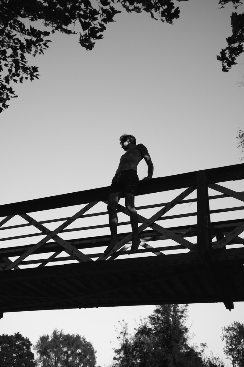 silhouette of topless man in shorts on bridge with tree against clear sky, male silhouette and bridge 4k