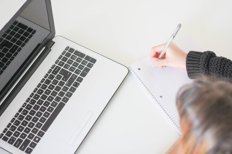 a woman taking notes in a large notebook next to a laptop, brainstorming 4k