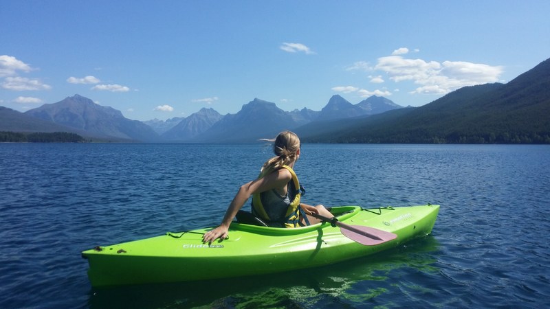 a young woman kayaking on a lake surrounded by low mountains in glacier national park, kayaking in glacier national park 4k