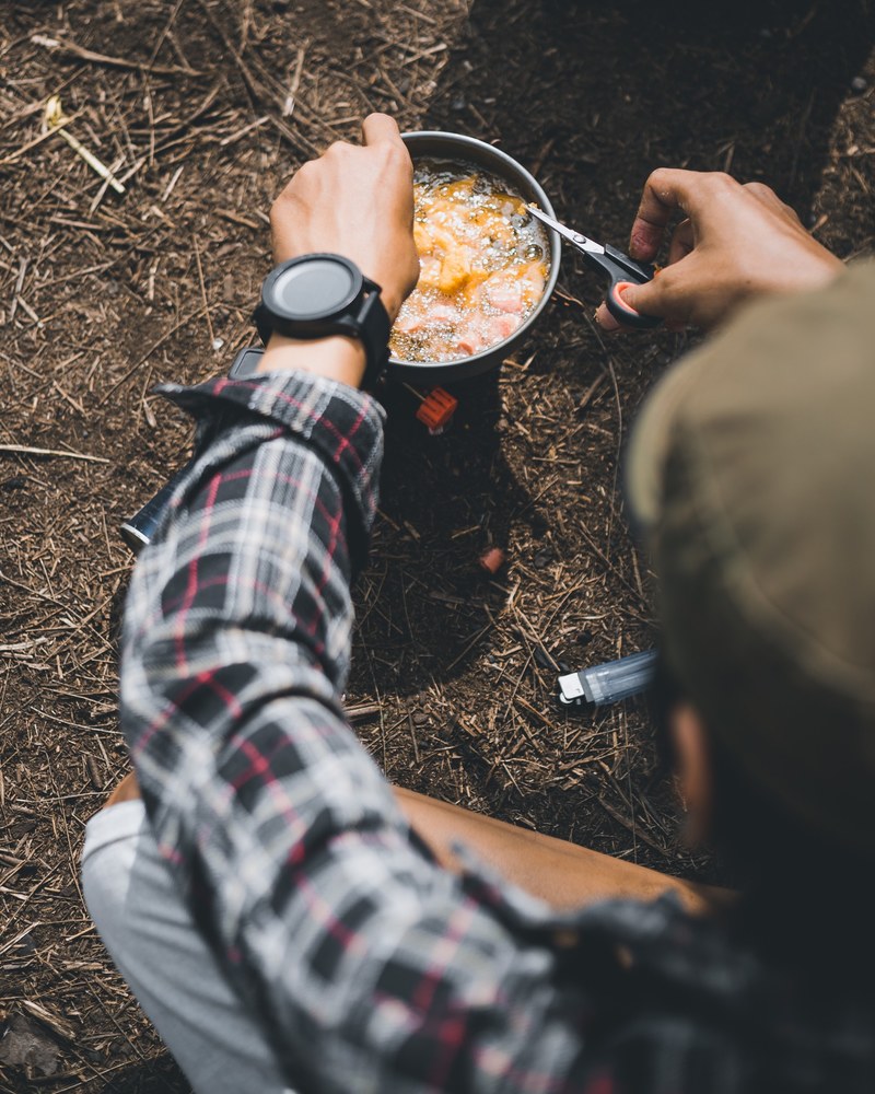 a man in plaid shirt wearing a watch is cooking on a camping stove in pacet, _cooking on a portable stove 4k