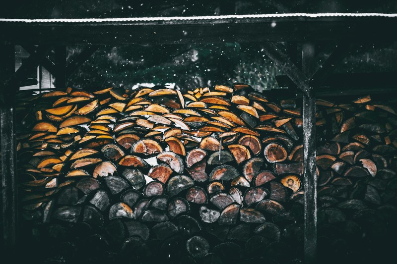 a stack of dark firewood under a snow covered roof, firewood shed in winter 4k