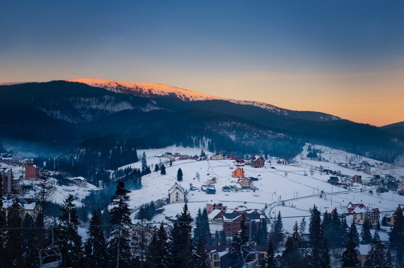 a ski lift in a village covered in snow on the edge of a mountain, bukovel mountain sunset 4k