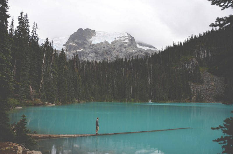 a man at a lake surrounded by trees and big rock covered in snow, walking on water in the woods 4k