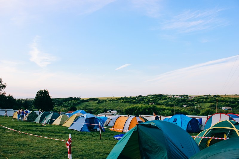 colorful tents are pitched along a grassy field with a bright blue sky behind thing, tent life 4k