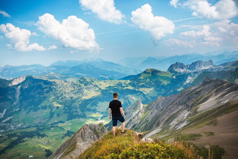 a male hiker standing on a grassy ledge overlooking a rural mountain valley, looking off into the countryside below 4k