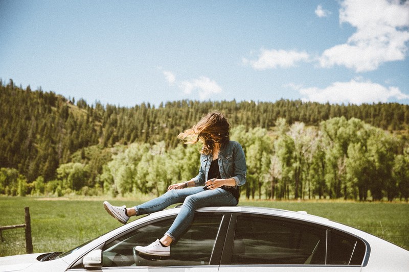 young woman in denim sitting on white car roof with evergreen forest in background, young woman in denim sitting on car roof 4k