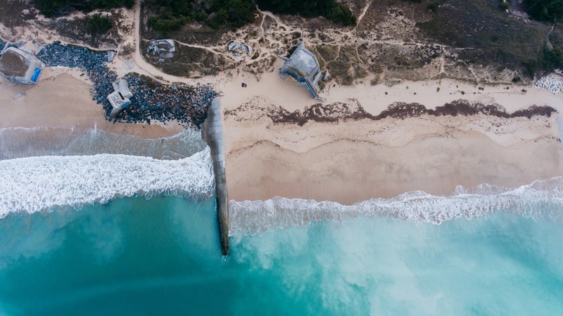 drone aerial view of concrete constructions on the sand beach at plage du petit bec, empty beach from above 4k
