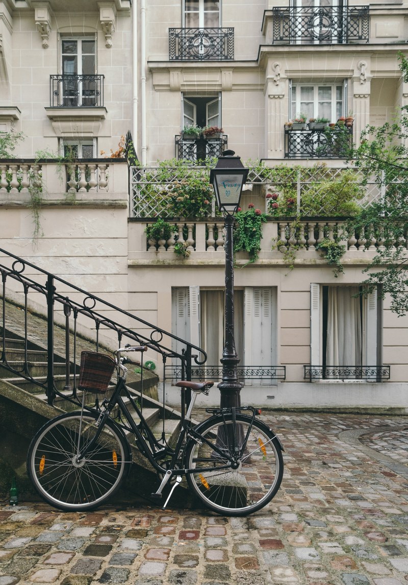 a bicycle resting against a flight of stairs and a lamppost with french buildings in the background, _bicycle with french buildings 4k