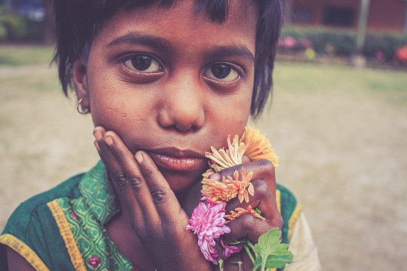 a close up of a little child holding colorful flowers close to her face, cross culture 4k