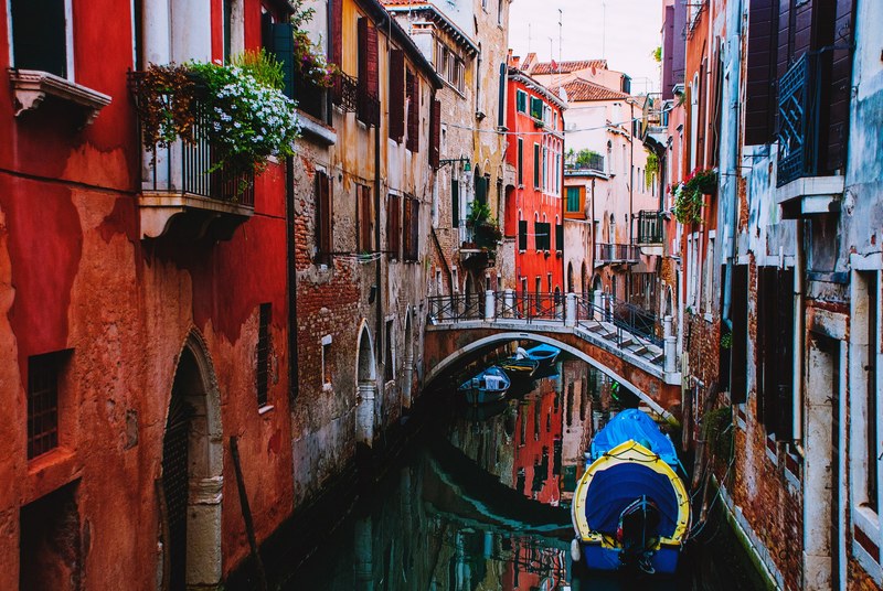 a canal with a bridge between red brick buildings in venice, red venice canal 4k