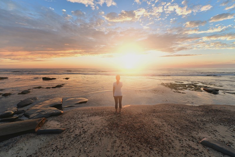 a woman stands on a calm shoreline with peaceful water and a clear sunrise with wispy morning clouds, woman shoreline sunrise_ 4k