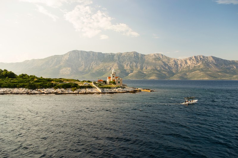 a building sitting on the edge of a sharp coastline with mountains in the background and a speed boat sailing past, _secluded mountain vacation 4k