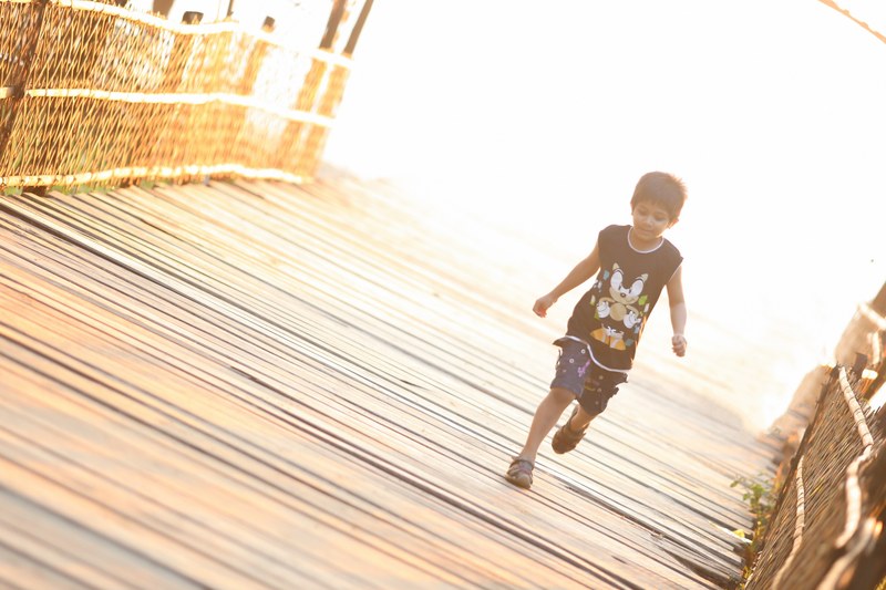 male child wearing a sonic t shirt and sandals running across a wooden bridge in bangladesh, child running across bridge 4k