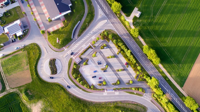 drone view on a parking lot by the roundabout surrounded by green fields and trees, drone view of the parking lot by the roundabout 4k