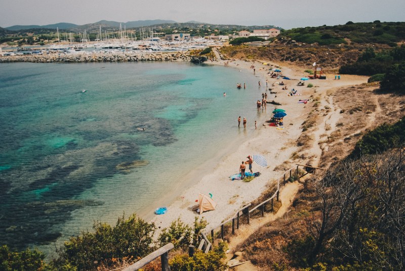 a group of tourists vacationing on a small beach near a waterfront in cagliari, vacation cove 4k
