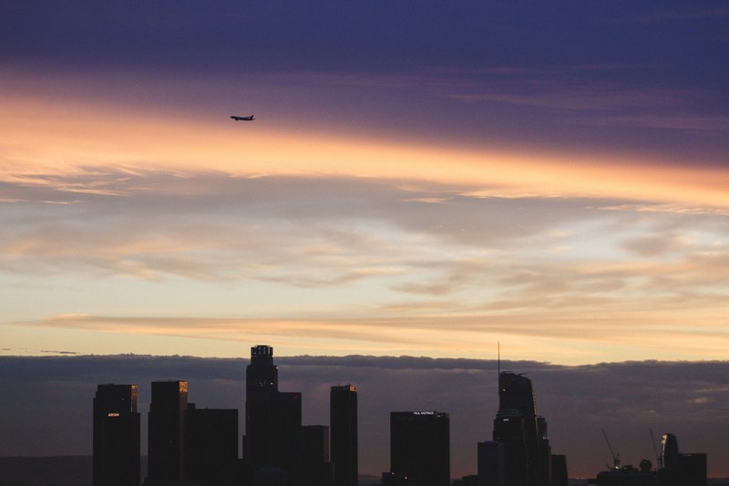 a plane flies over los angeles in front of a cloudy sunset, busy but subtle 4k