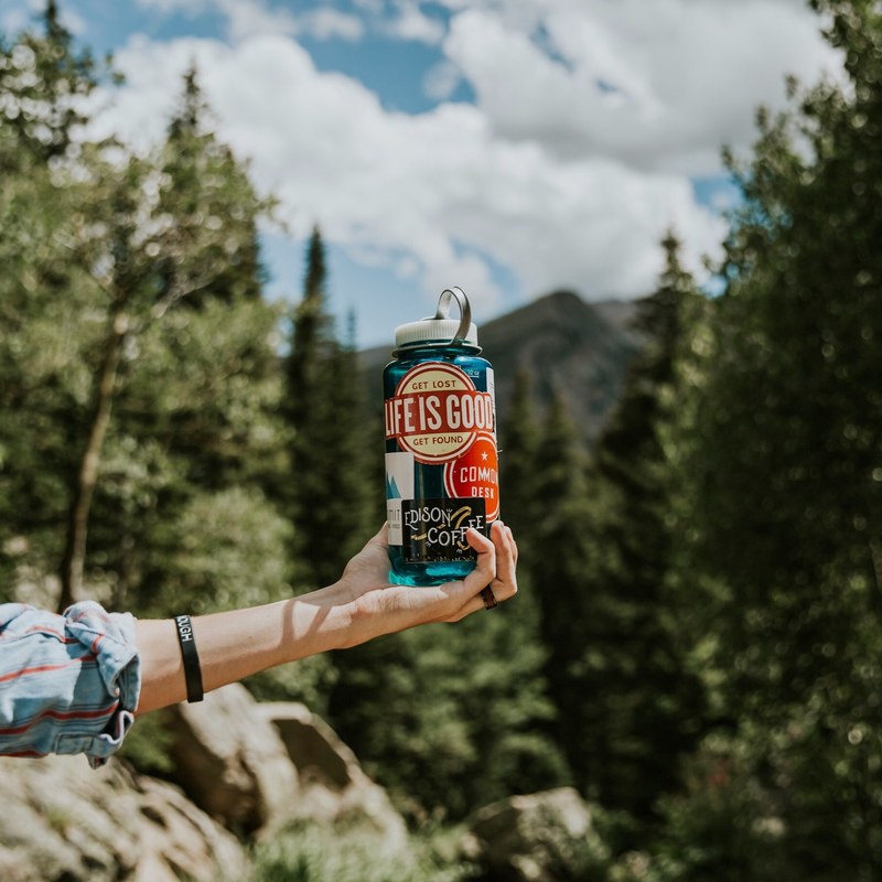 hand holding canteen reached out over rocks and trees with mountain in background, hand holding bottle 4k