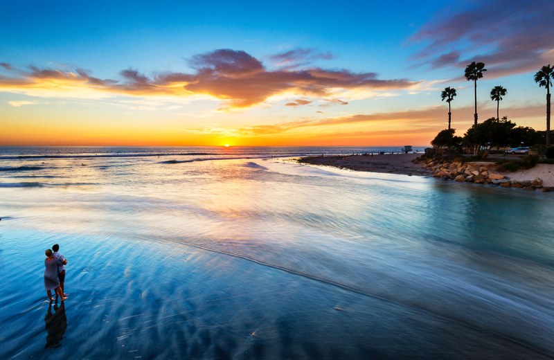 aerial view of couple embracing in cardiff during sunset with the sandy beach and palm trees in the horizon, summer evening 4k