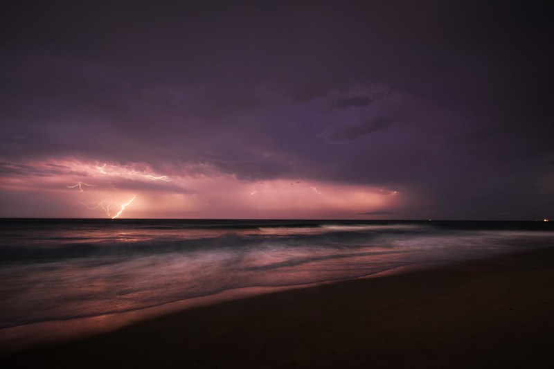 a bolt of lightning erupts from the clouds during a purple sunset over the southern shores, lightning crashes 4k