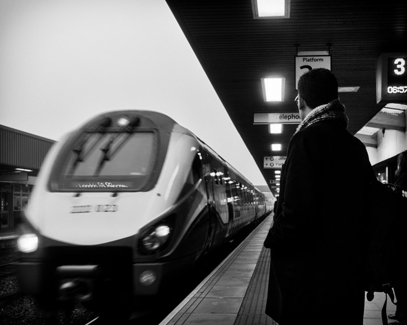 black and white behind shot of man in coat with scarf standing on leicester train platform, on the way to work 4k