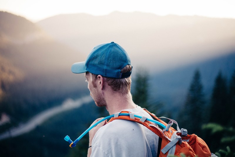 a man in a cap and orange backpack hikes in the mountains at stevens pass, wear deet 4k
