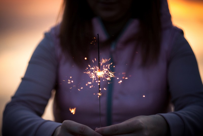 a woman in a hoodie holds a lit sparkler in her hands, woman holding sparkler 4k