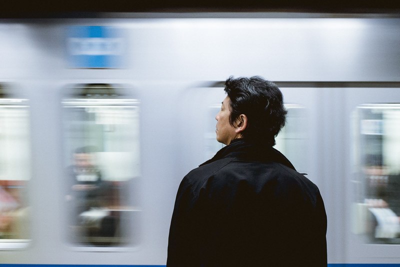 a man waits at the edge of the platform as a train arrives at the station, waiting for the train 4k