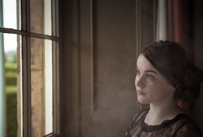 a young woman with brown pulled back hair looks out a window, woman looking out a window 4k
