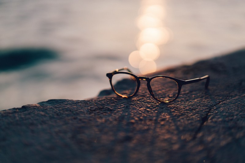 a pair of glasses sits on a rocky surface by a body of water, sunset view 4k