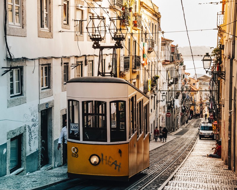 yellow tram carriage suspended at the top of a narrow street with traditional architecture lisbon portugal, up 4k