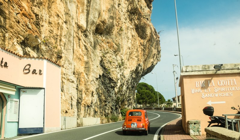 a vintage red car driving down a windy road on the side of a cliff, _on the border to italy 4k