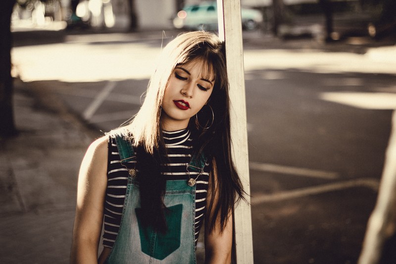 woman in a trendy outfit leaning against a post with her eyes closed, finding a quiet moment 4k