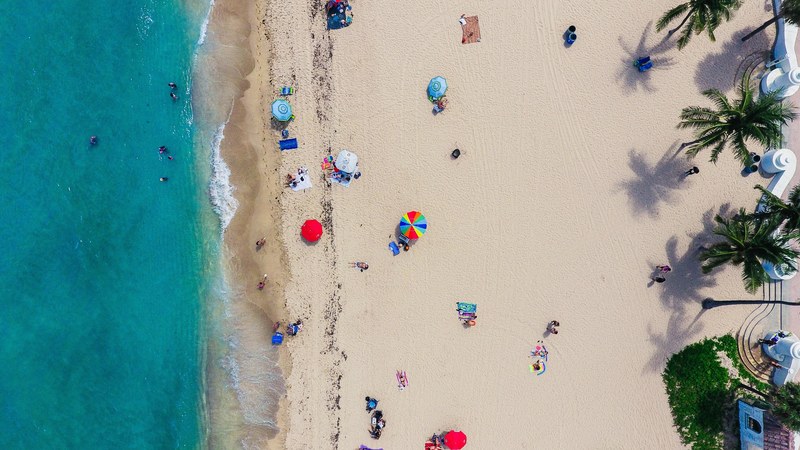 an aerial shot of tourists sunbathing on the sand and swimming in the ocean, golden beach in birds eye view 4k