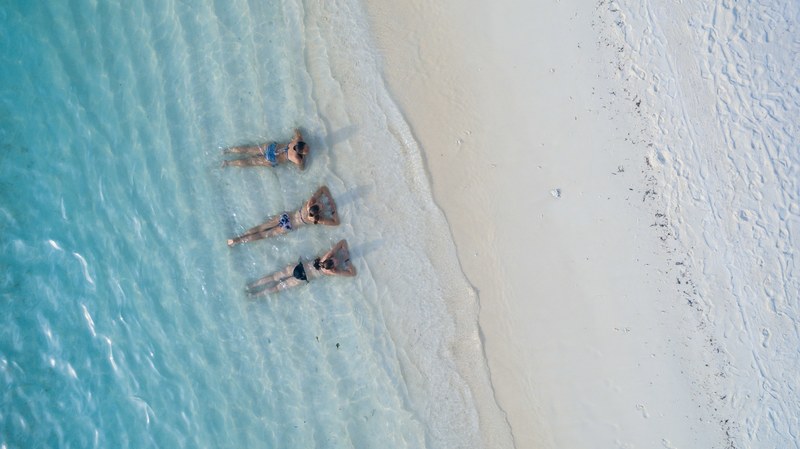 a drone shot of three women lying in shallow water on the beach and sunbathing, relax 4k