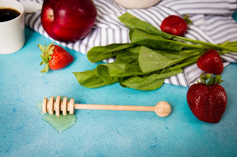 wooden honey dipper stirring rod on a blue surface next to leaves apples strawberries and a mug of coffee, honey dipper stirring rod 4k