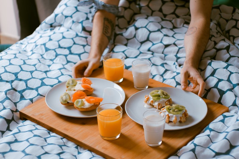 a person holding a platter of bagels and waffles over a bed in barcelona, breakfast in bed 4k