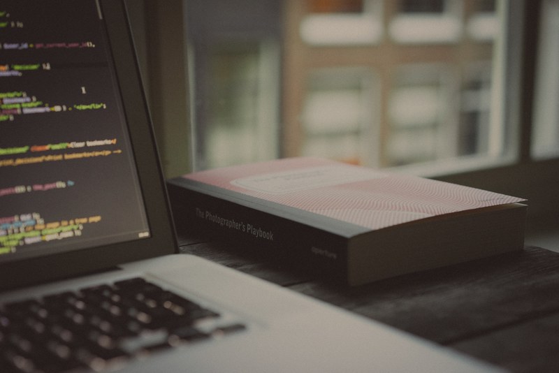 the photographers playbook on a desk next to a laptop with lines of code on its screen, two loves 4k
