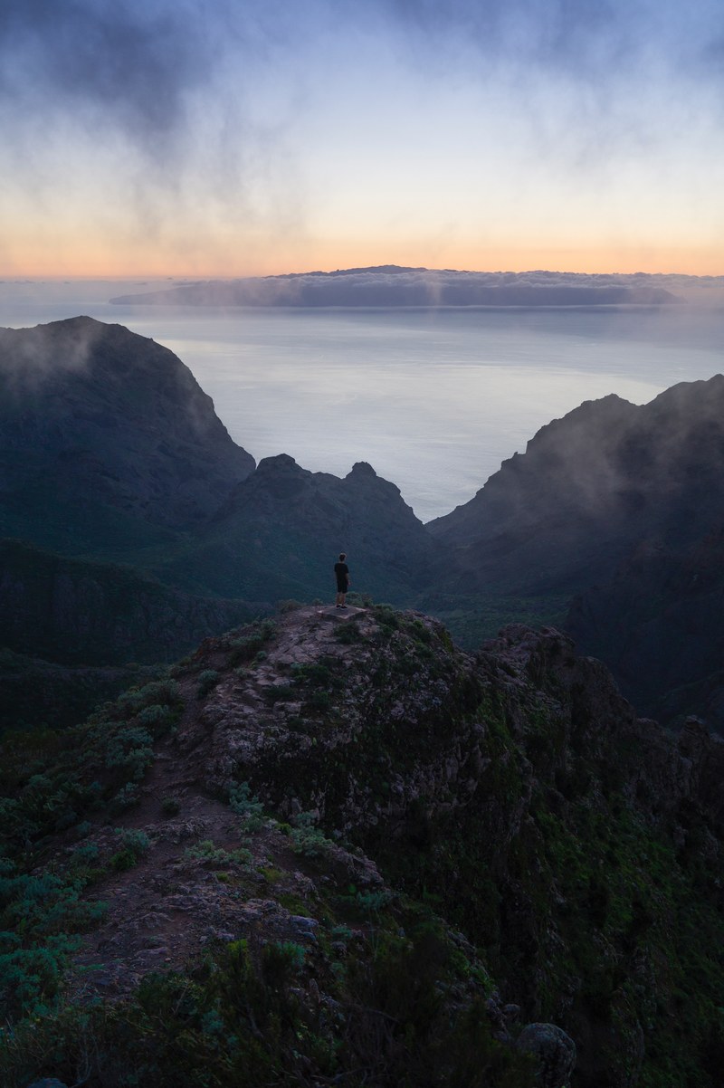 hiker stands on a rocky mountain peak on a foggy day in masca, misty hikes in masca 4k