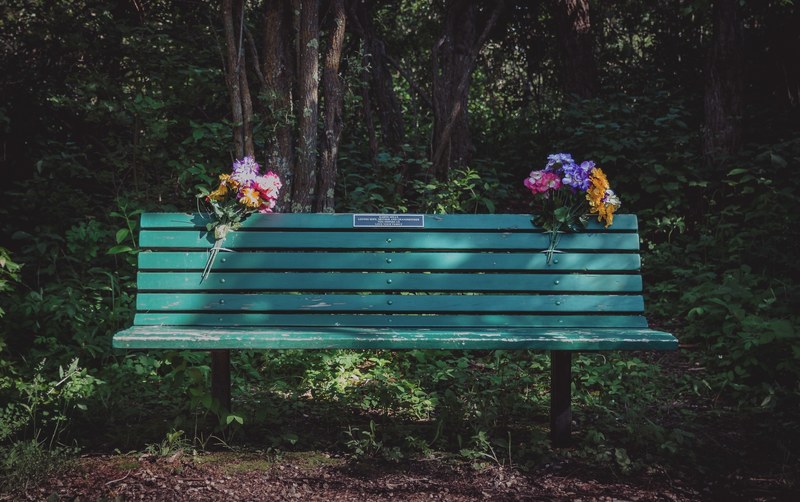 two colorful flower bouquets attached to a green park bench with a plaque on it, immortalized 4k