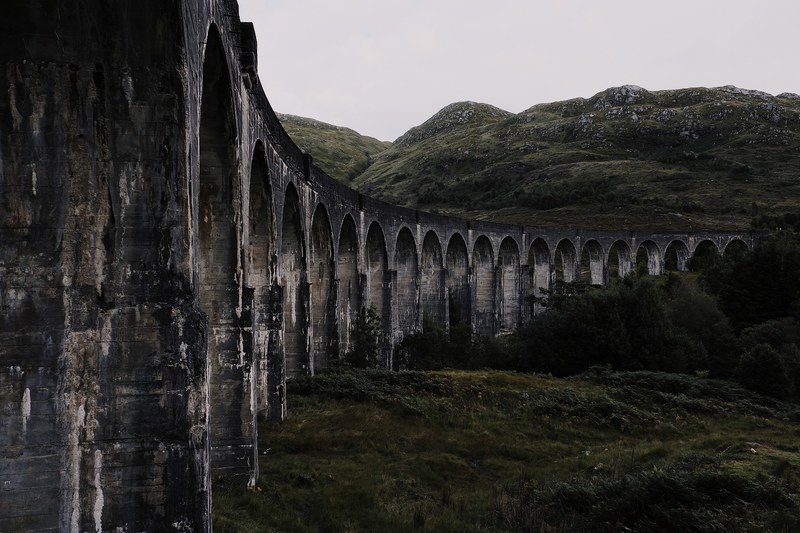 run down concrete bridge through a lush country field, glenfinnan viaduct 4k